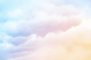 A blue sky background dominated by fluffy white coulds that have hues of orange, pink and purple. Clouds reflect a faded rainbow.