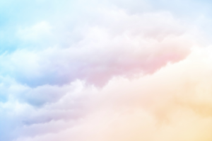 A blue sky background dominated by fluffy white coulds that have hues of orange, pink and purple. Clouds reflect a faded rainbow.