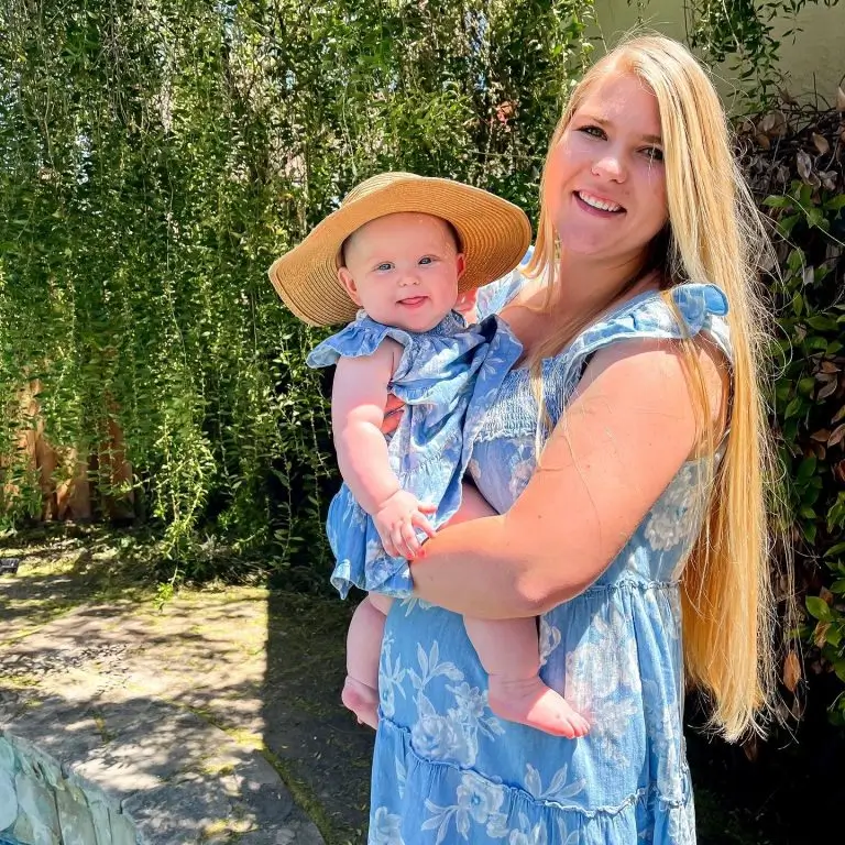 Woman with long blond hair and wearing a blue dress holding a baby