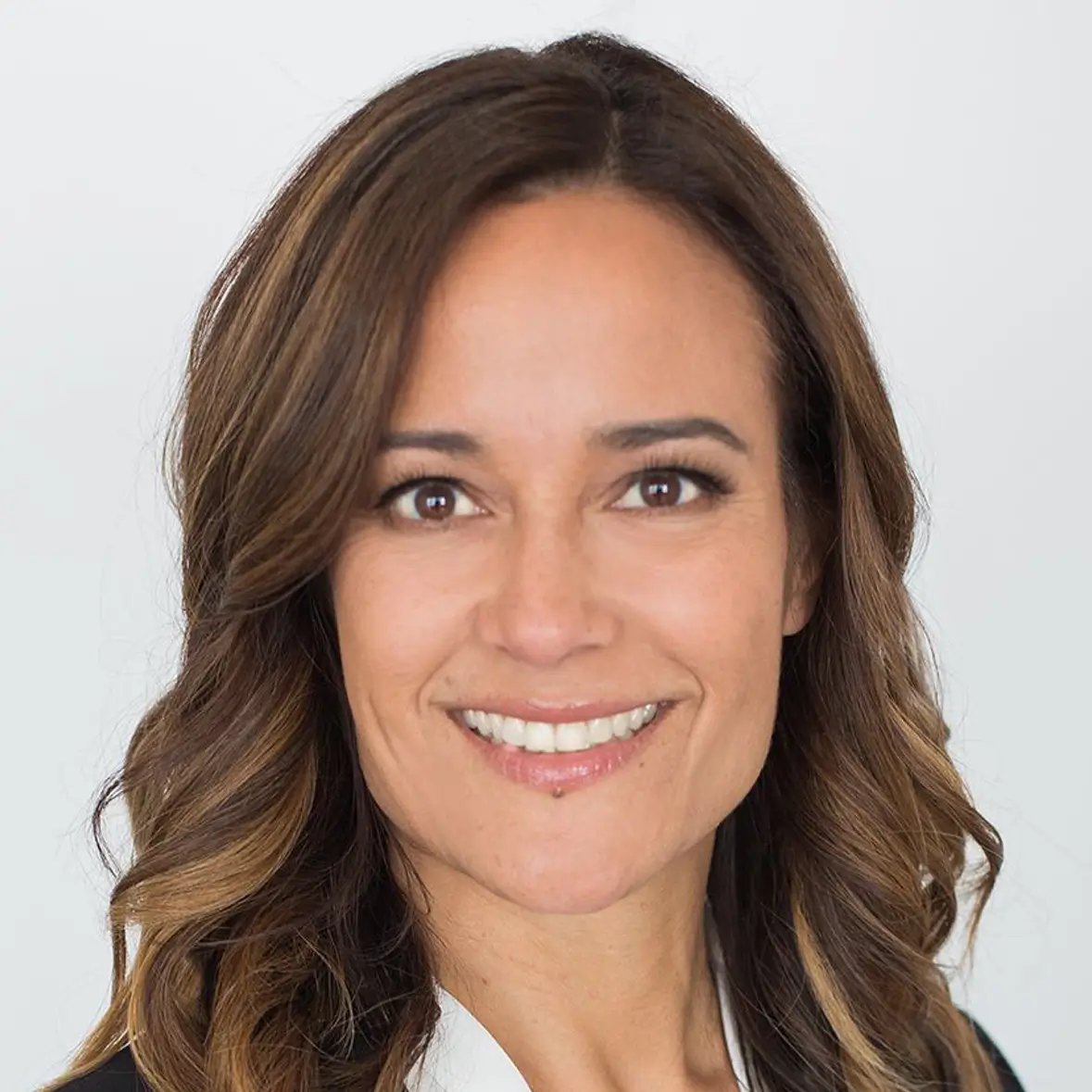 Smiling woman with shoulder-length wavy brown hair, dressed in a suit.