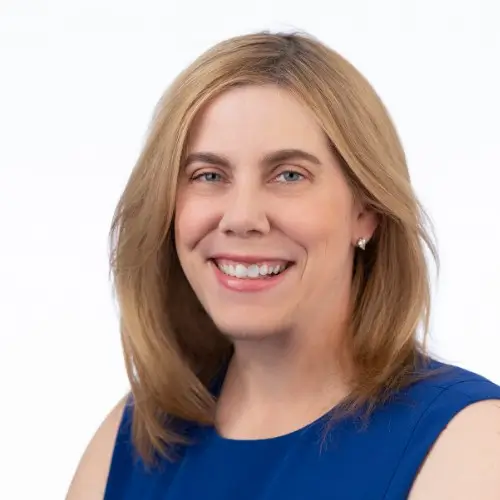 Woman with shoulder length blonde hair and blue sleeveless top smiling.