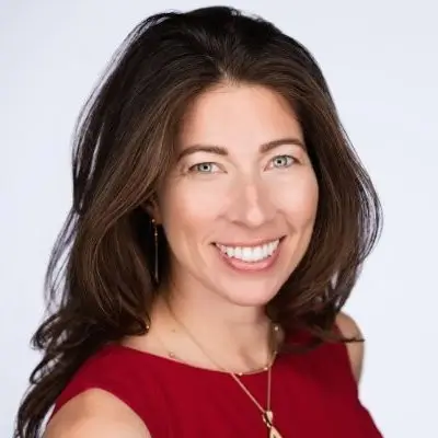 Portrait of Monica Phillips, smiling, wearing a red sleeveless top with long dark hair, against a plain white background.