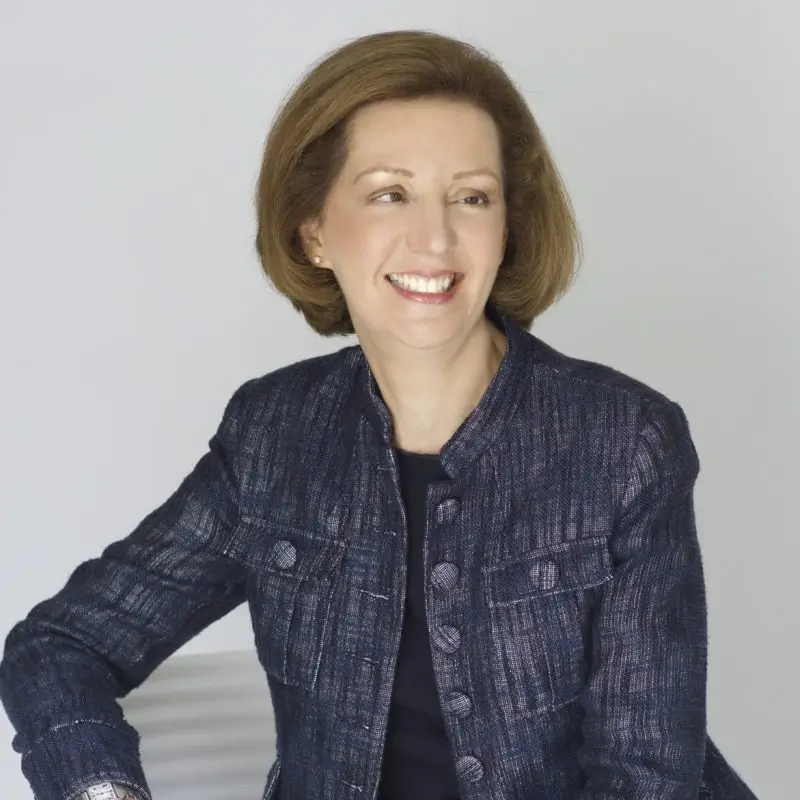 Portrait of Bridget Sheridan-Johnson, smiling, wearing a dark textured jacket with a light background.